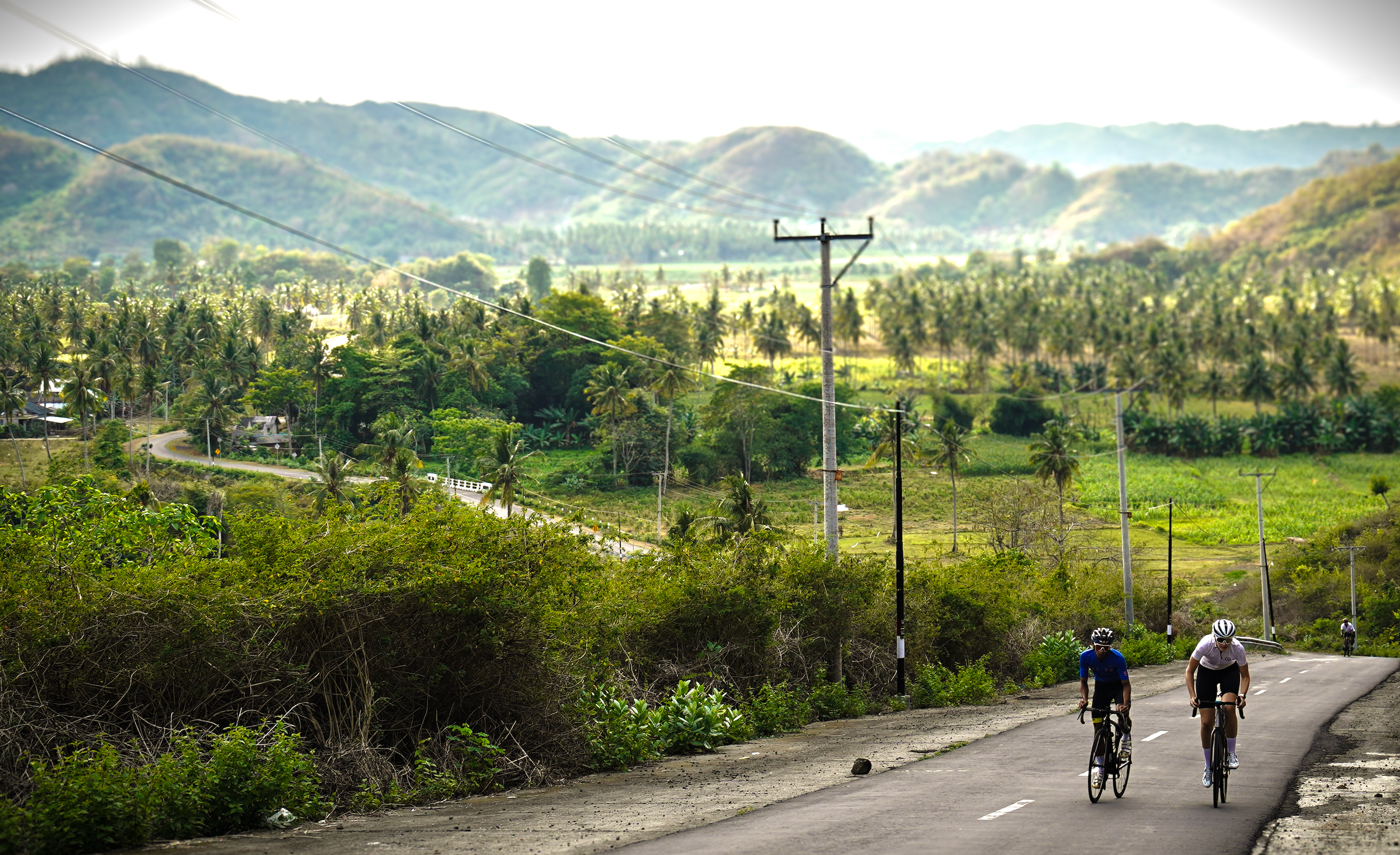 Qunafa cyclists on a road with a scenic background of hills and greenery. in Lombok, by Qunafa Travel tour Guided Adventure