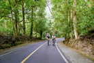 Group of cyclists descending a scenic Bali road with ocean views — Qunafa Travel guided tour